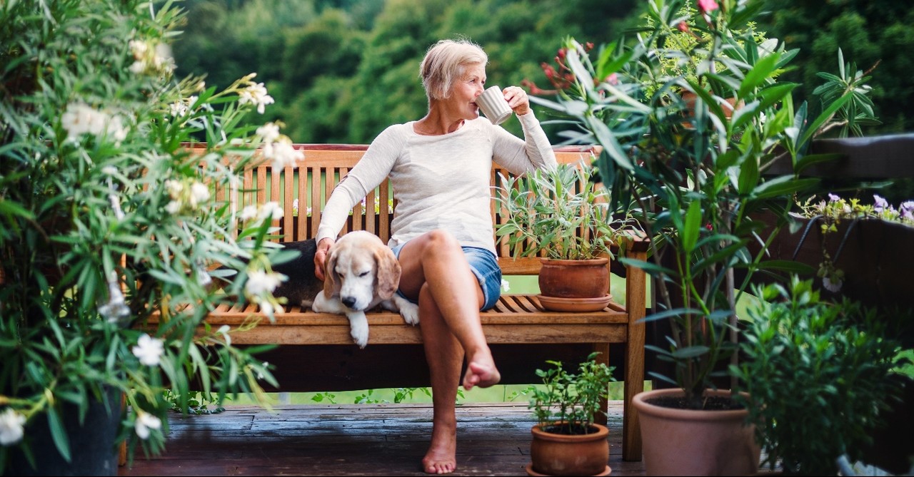 Elder woman drinking coffee with her dog in her garden