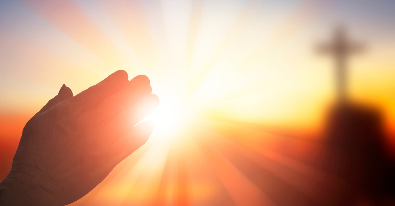 praying hands at sunset with cross in background