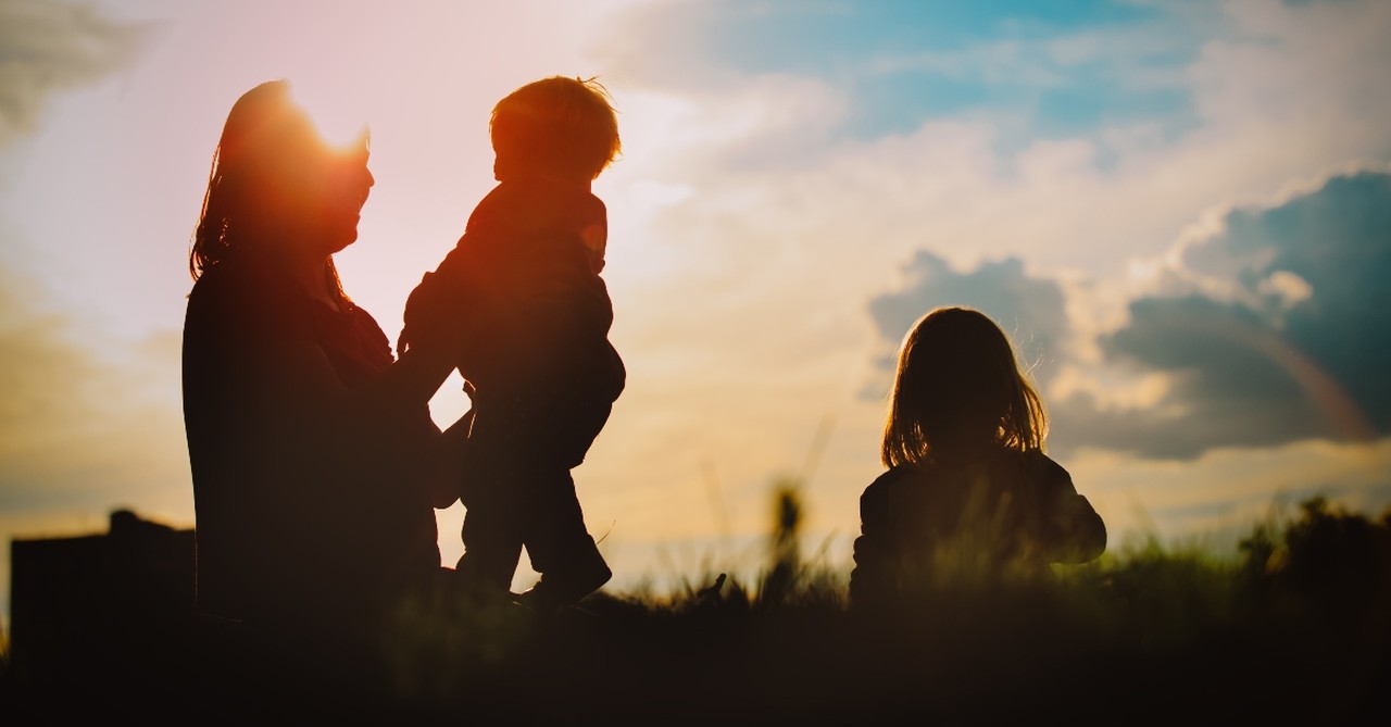 silhouette of mother with children sitting in grass outside happy, prayers for peace in the family