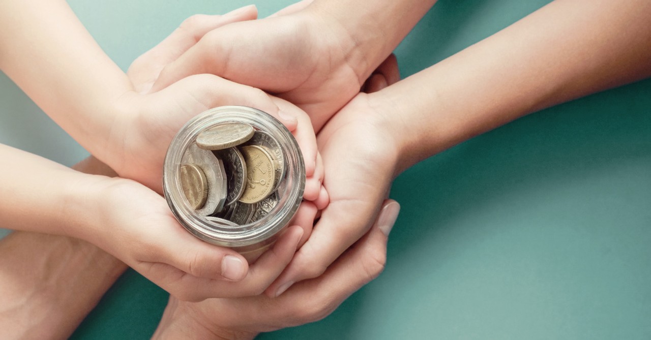 Several hands holding a jar full of coins