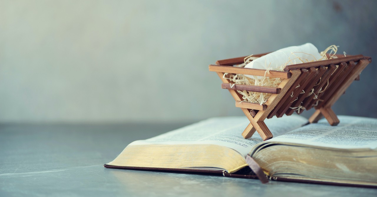 Small wooden nativity manger sitting on top of open Bible, the Word became flesh