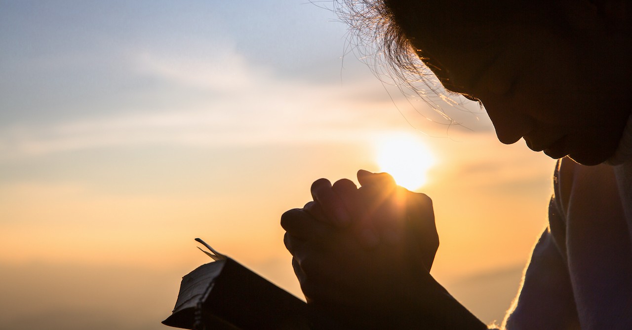 Woman praying over Bible outside at sunrise, good things come to those who wait