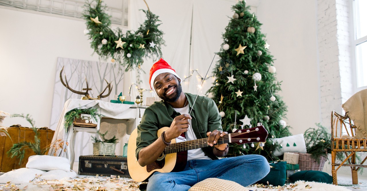 man wearing santa hat and holding guitar with Christmas tree