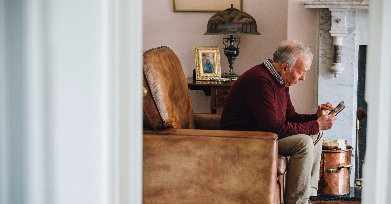 An elderly man looking sadly at a picture frame