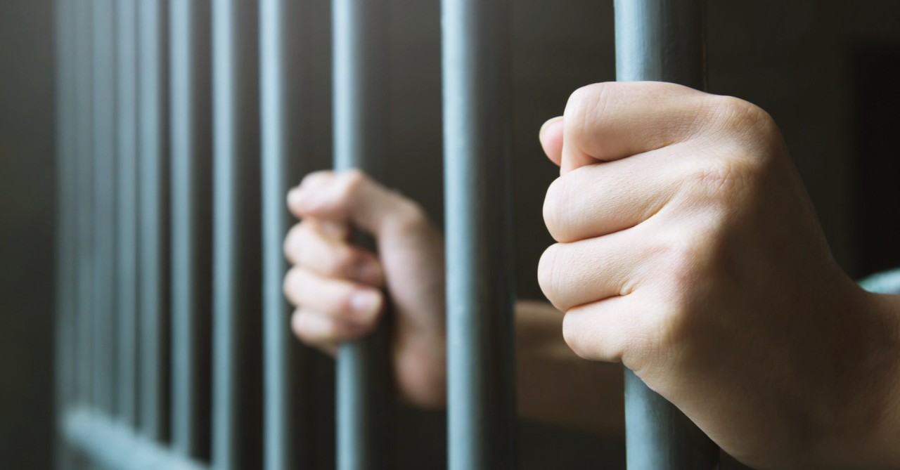 Hands holding the bars of a jail cell