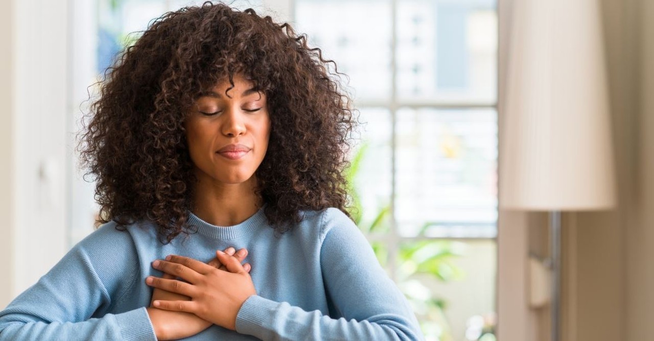 woman with eyes closed at table with hands over heart peacefully