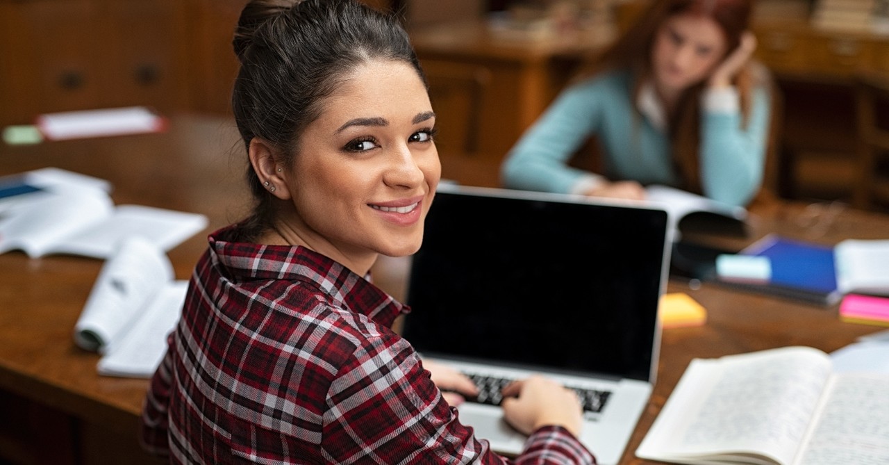 female college student smiling and studying in library on computer