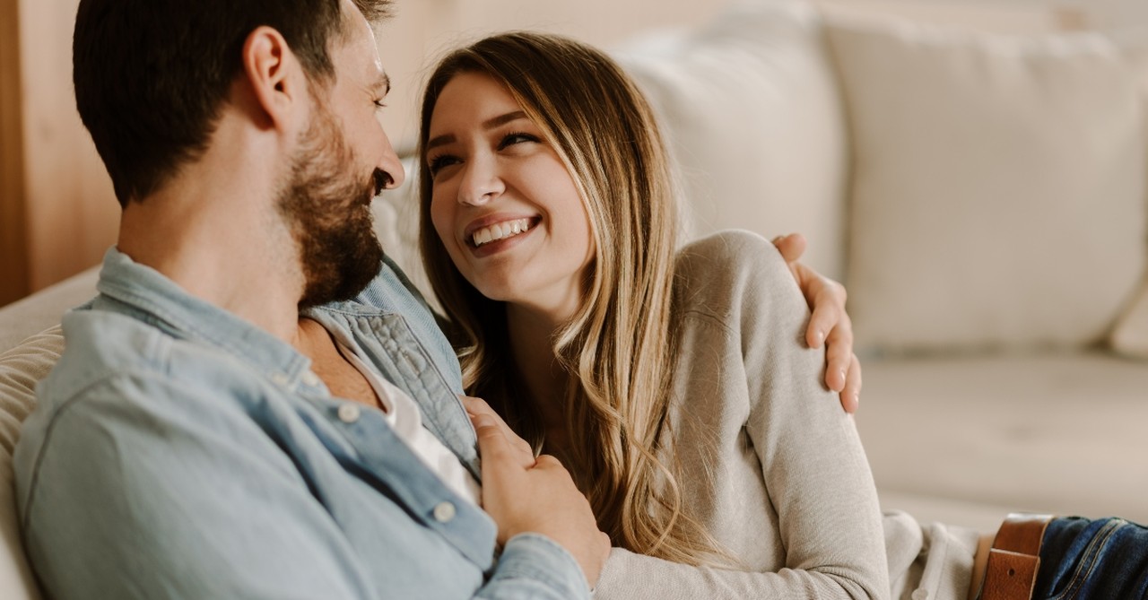 young couple sitting on couch together looking happy, how to be husband wife needs