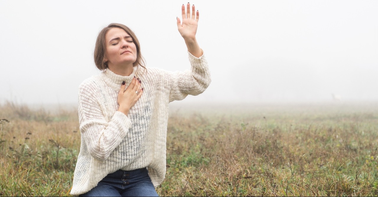 Woman kneeling in prayer with her hand up