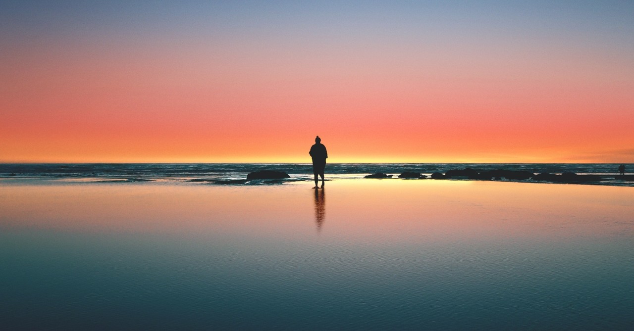 man standing on shore at night under colorful sky alone