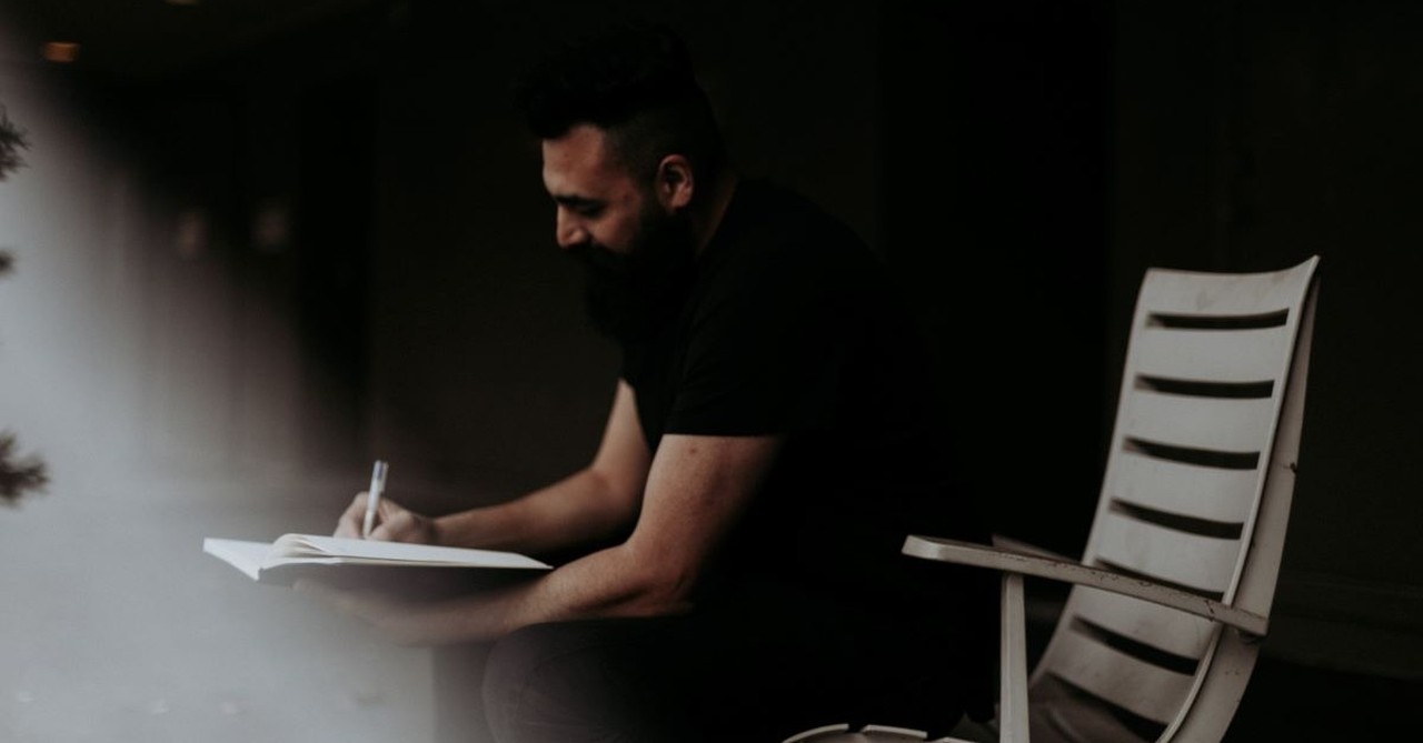 man writing journal journaling sitting all black smiling focused