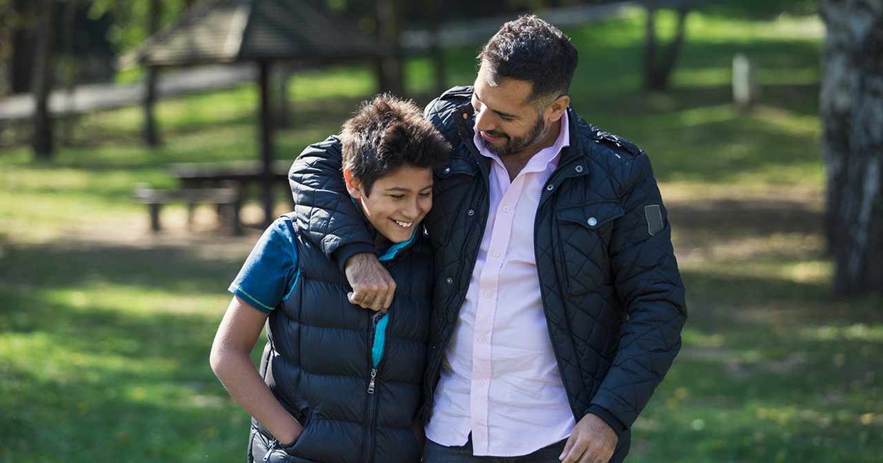 A smiling father and son walking and talking together outside