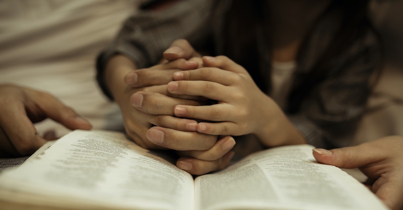 parent and child with prayer hands on open Bible