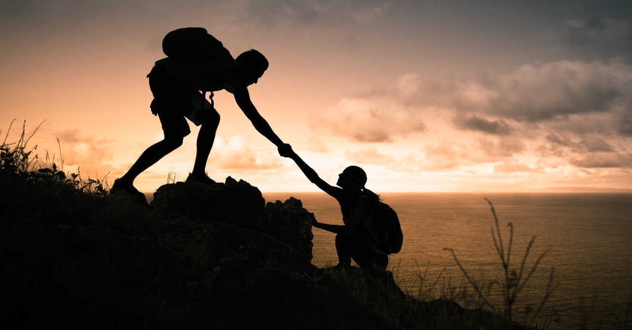 Woman pulling man up on a mountain