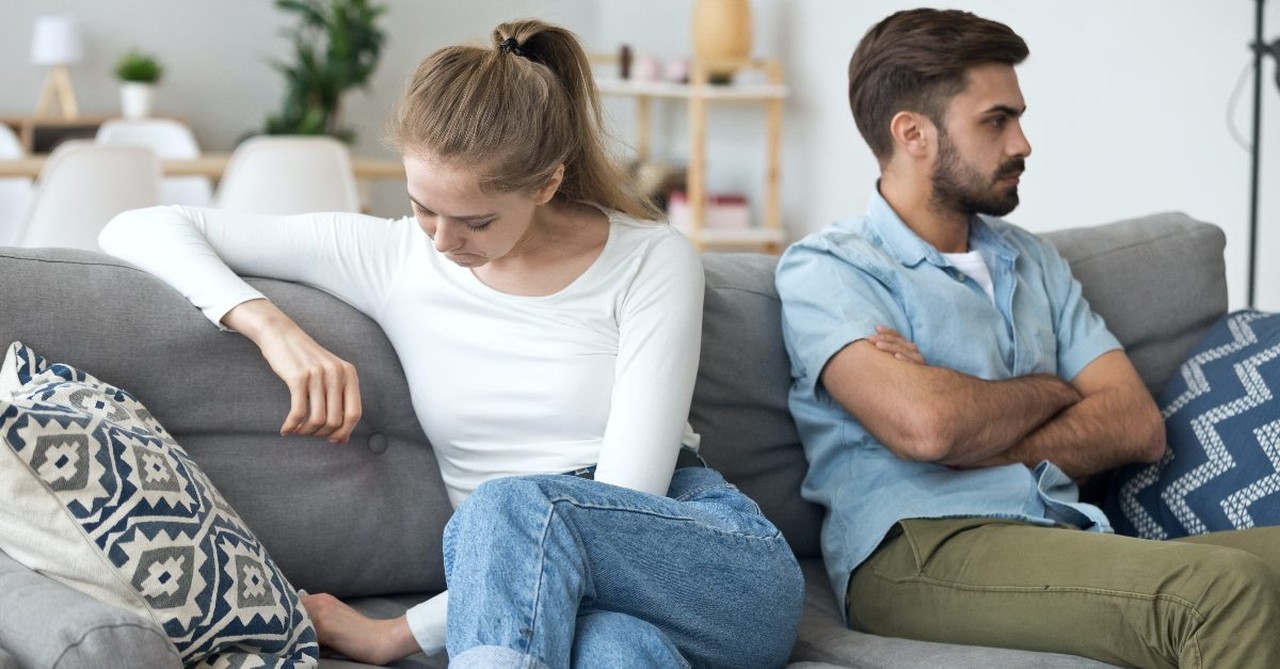 A sad man and woman sitting on a couch ignoring each other