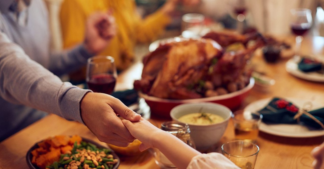 At Thanksgiving dinner a family holding hands while praying, thanksgiving food