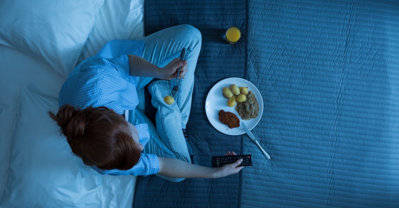 Woman eating dinner alone in bed, watching TV