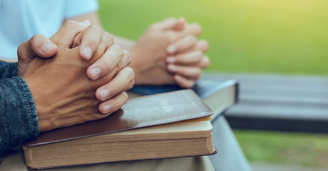 Two hands praying on Bibles