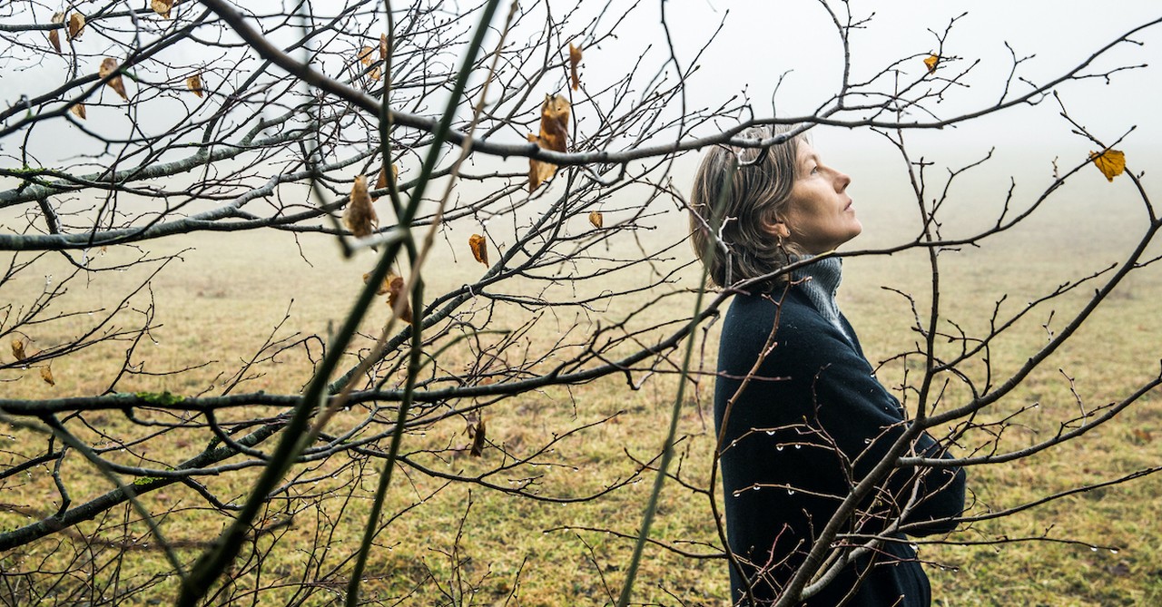 sad woman standing outside under a tree losing its leaves