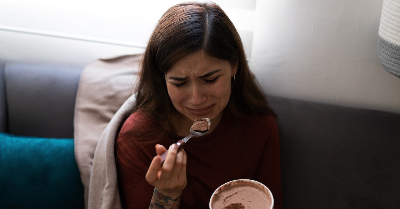 Sad crying woman on couch eating ice cream break up