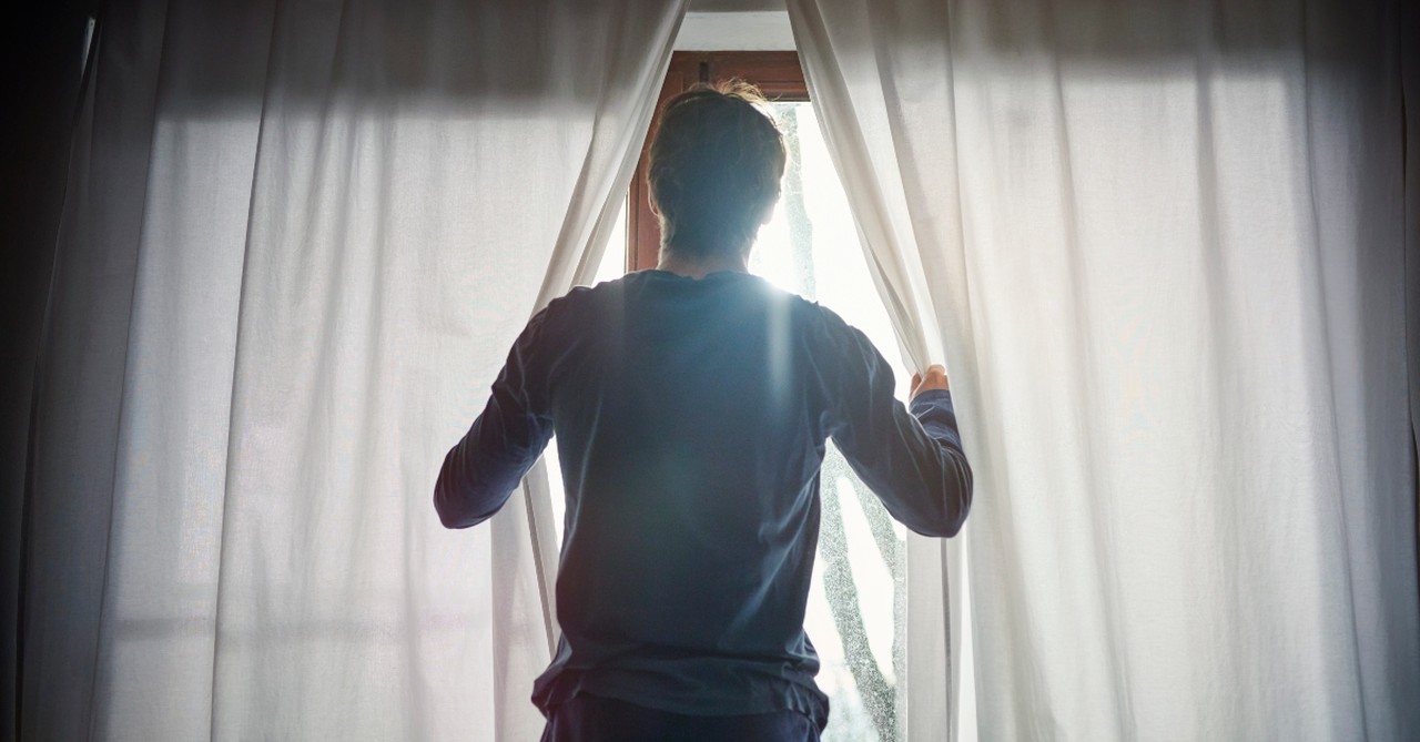 Man looking through curtains out the window