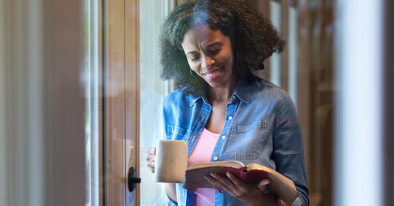 woman reading Bible in one hand and holding coffee in another