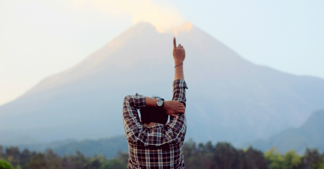  back view of man pointing finger on one arm up to sky in worship of God