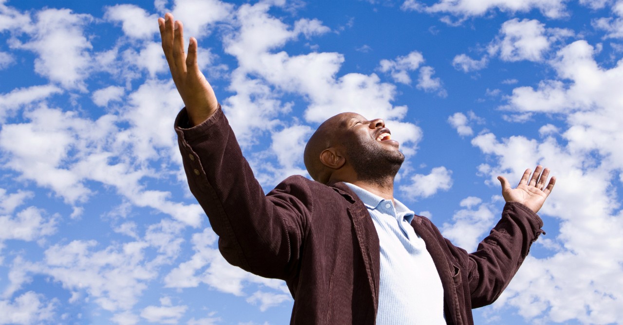 man with arms out wide in praise up toward blue sky