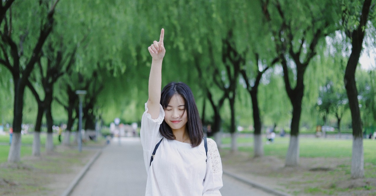 young asian woman with eyes closed pointing up in praise and honor of God in outdoor park