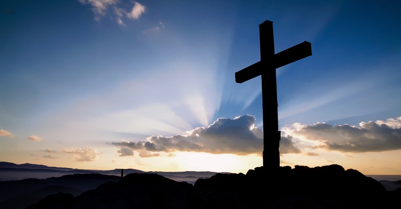 upshot of cross silhouetted against sunrise