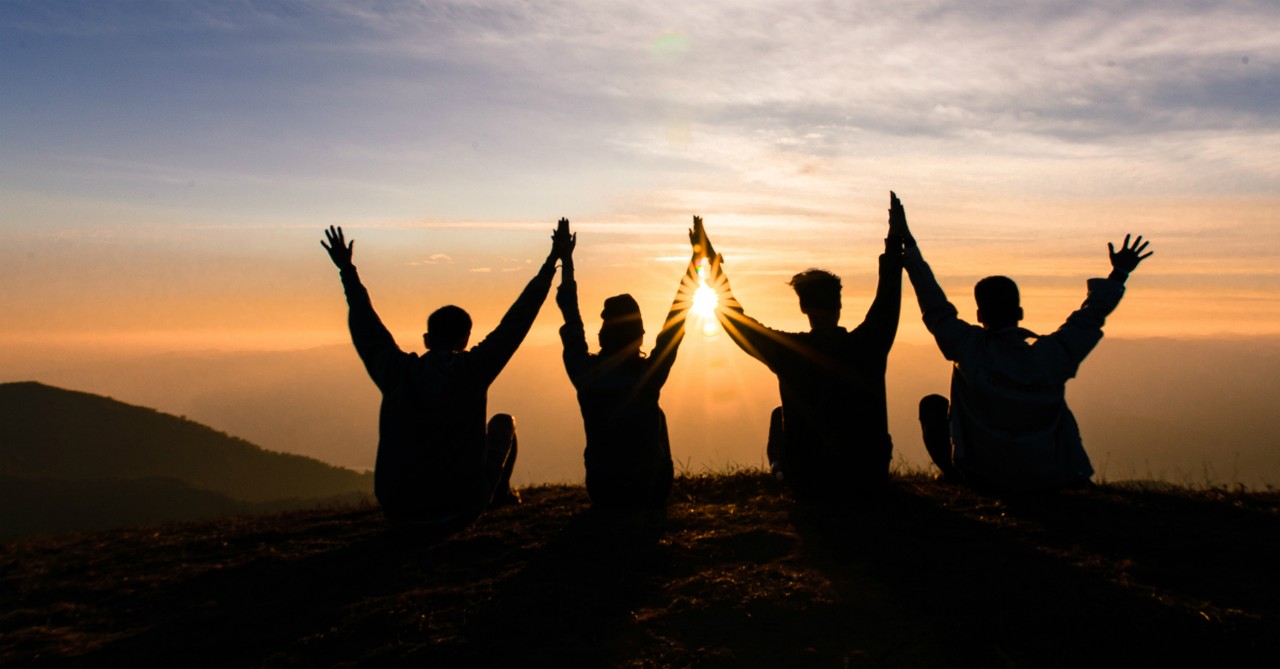 friends with hands raised before sunset