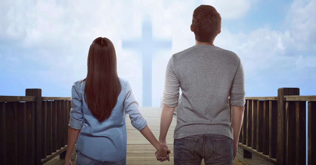 young couple holding hands looking at cross