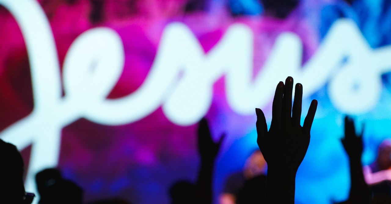 worshipping in church with lit up Jesus sign on stage