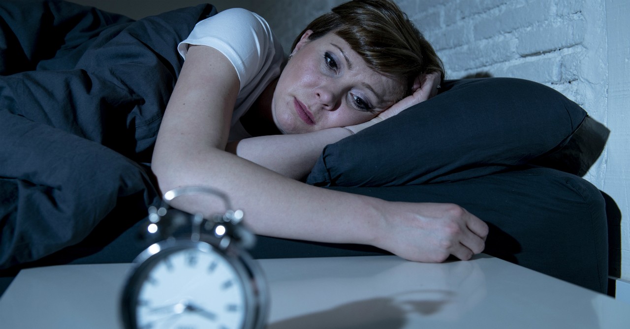 woman staring at clock, unable to sleep