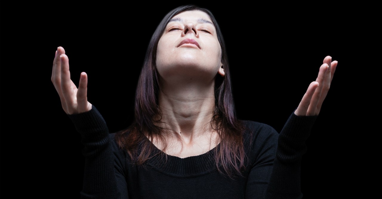 woman with eyes closed face up hands held up in prayer