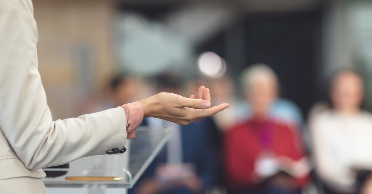 A woman speaker gesturing before a crowd