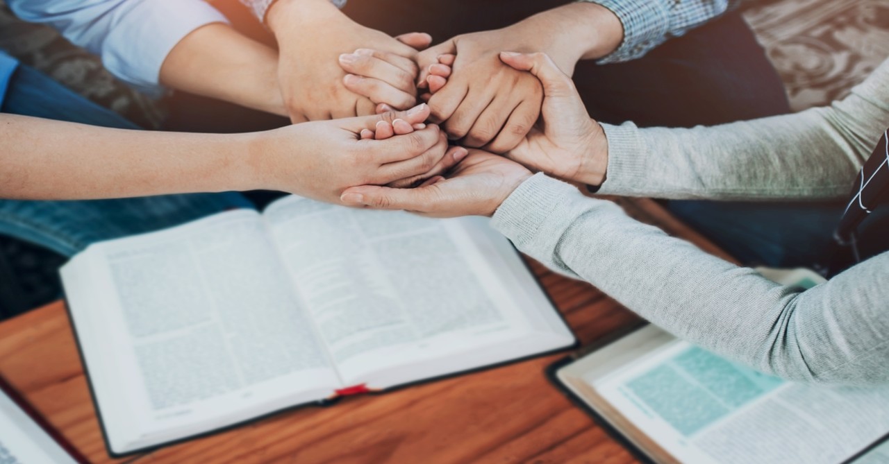 people holding hands over bible