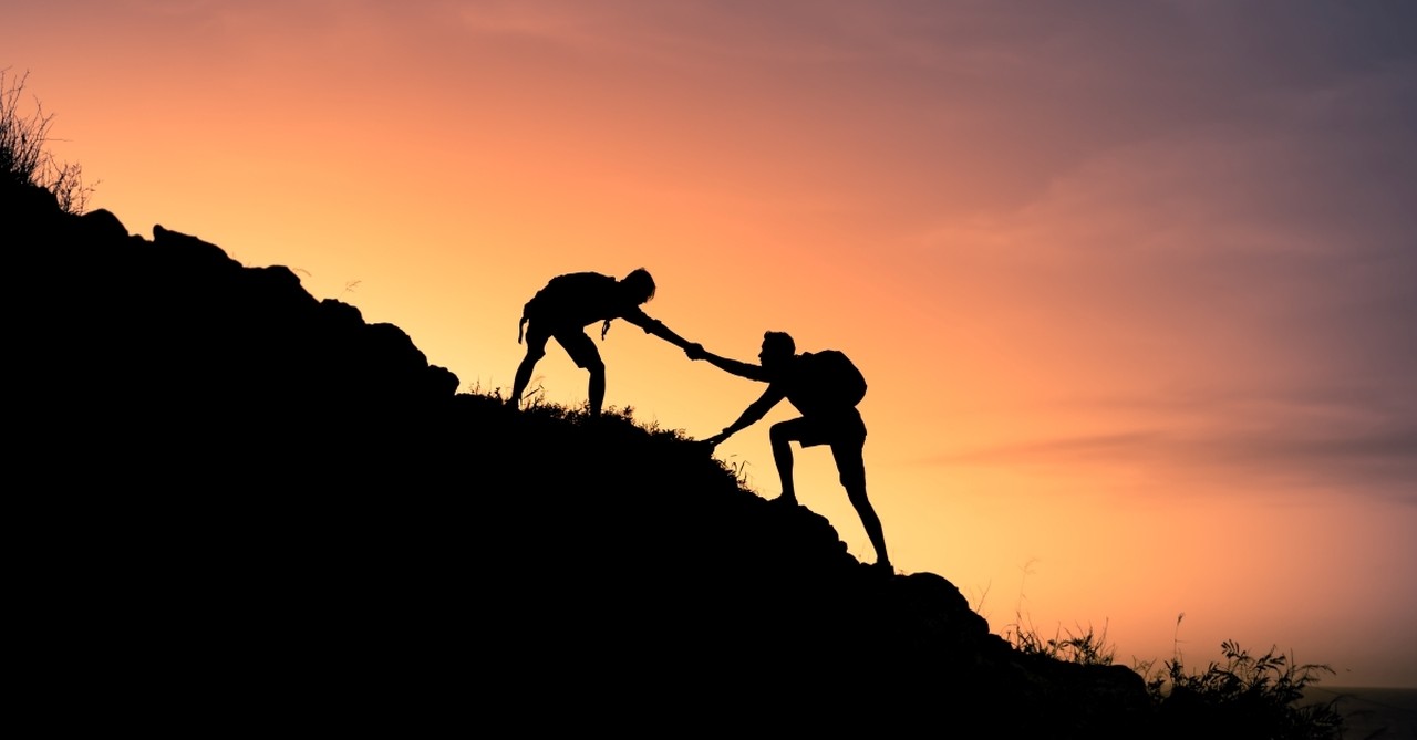 hiker helping another hiker up mountain