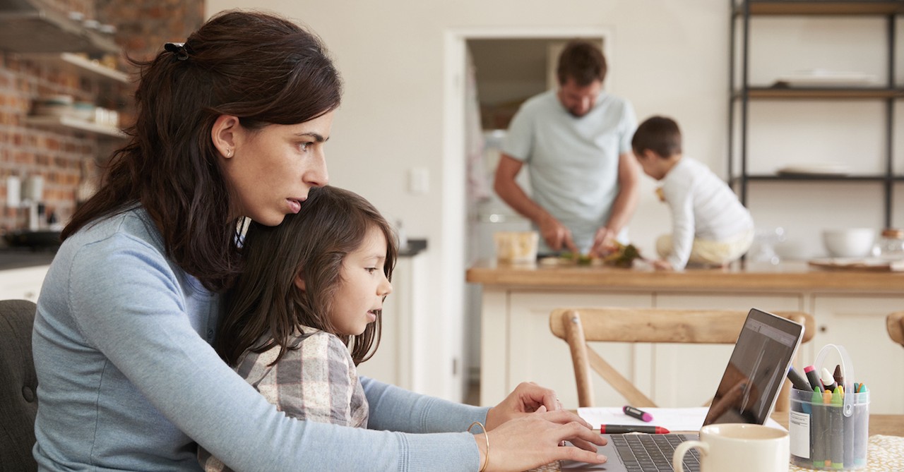 Busy mom working at home on laptop with family