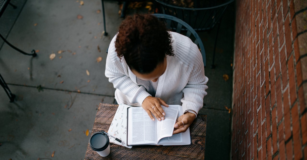 view looking down at woman reading Bible outside at table