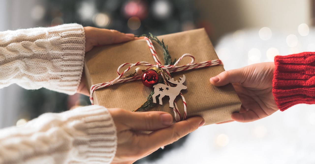 A person handing over a beautifully wrapped Christmas gift