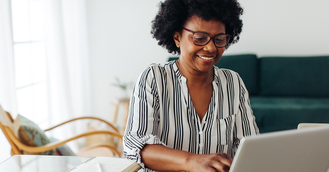 A mature, smiling woman works from home on her computer