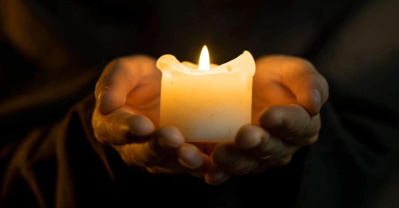 Hands holding a small lit candle