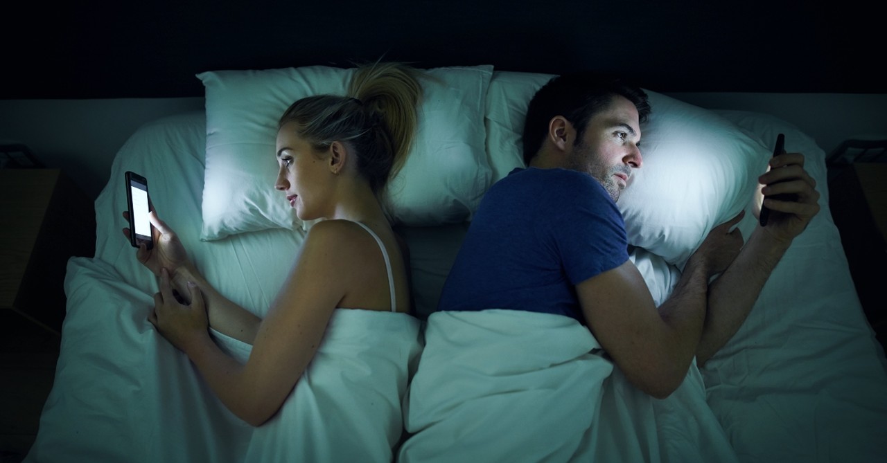 Wife and husband looking at their phones in bed