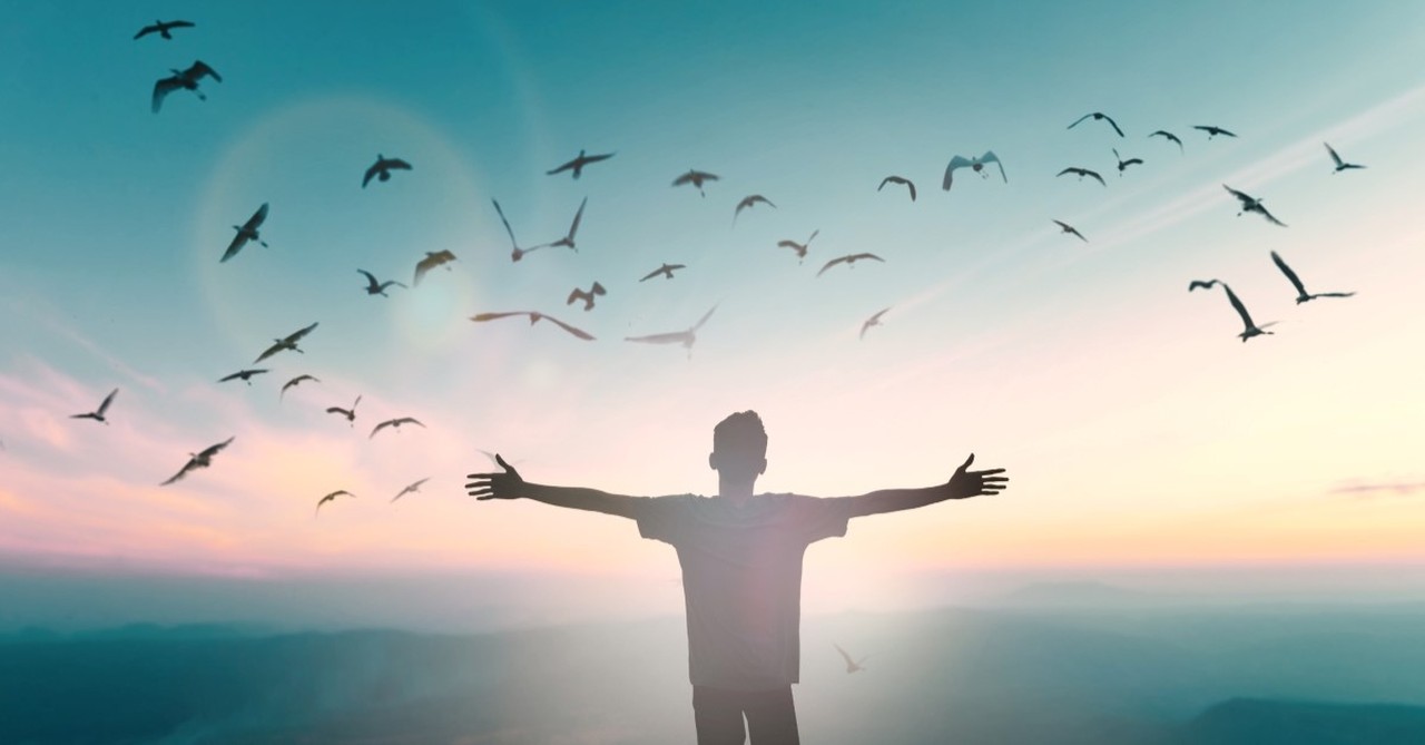 happy man standing on cliff with hands raised, god shows up in our darkest hours