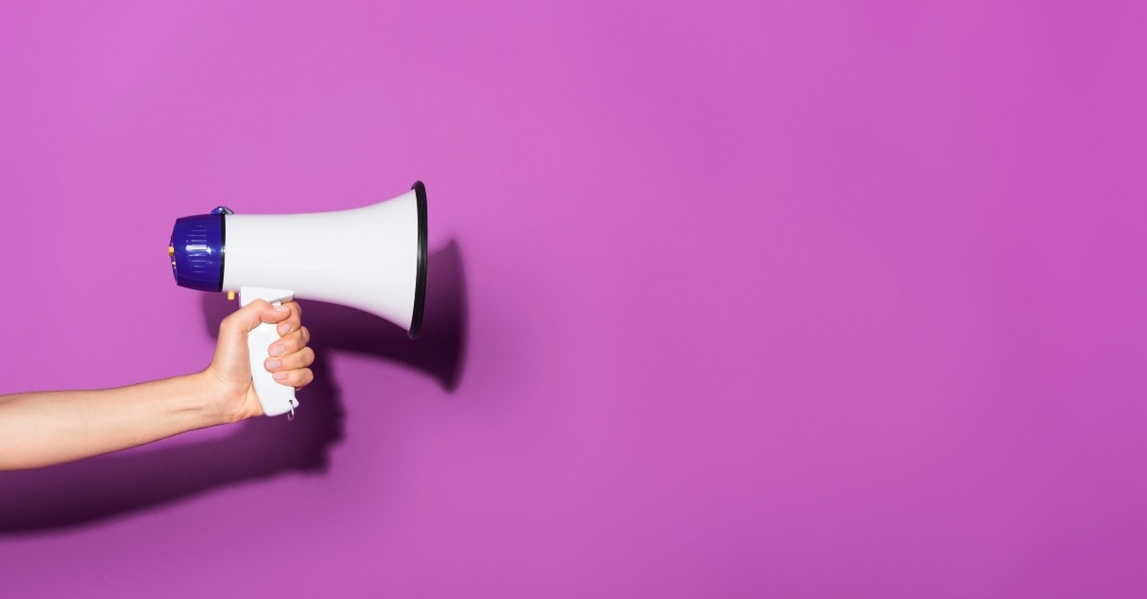 A person holding out a megaphone against a purple backdrop