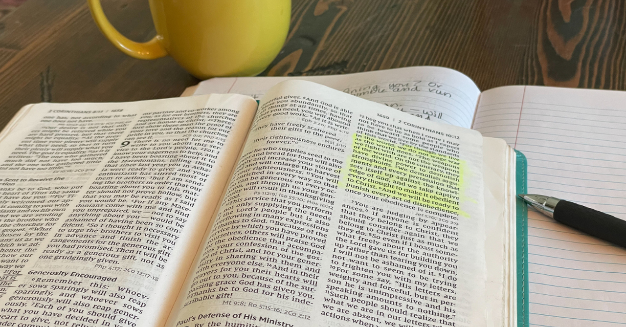 Open Bible with yellow coffee mug and notebook and pen on a table.