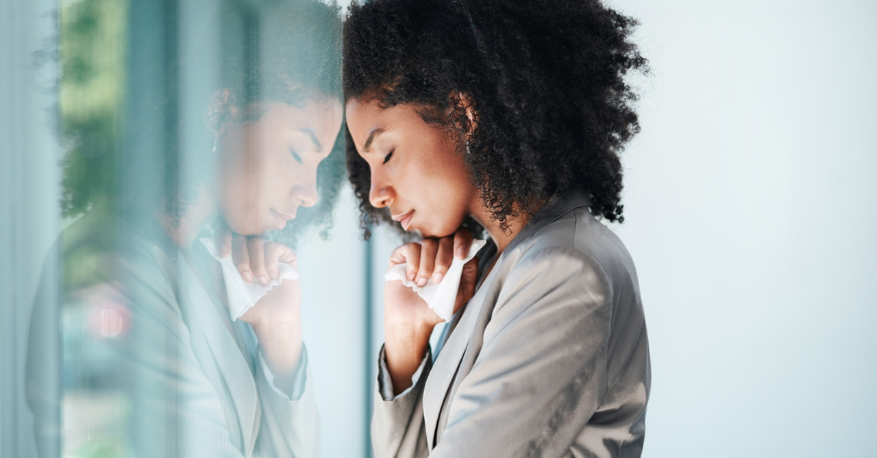 Woman leaning up against a glass door, crying.