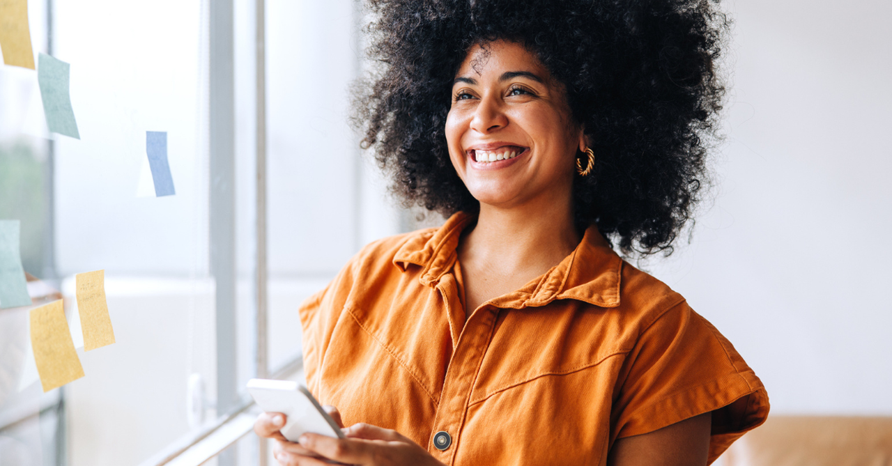 Woman smiling, holding her phone at work, fully present.