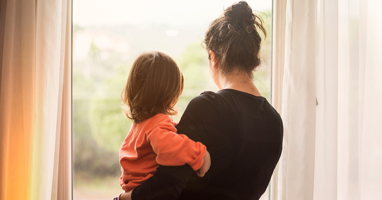 Mom, holding her child, both looking out the window, missing loved ones